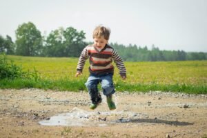 A cheerful child in a striped sweater jumps into a puddle on a sunny day in Czechia.