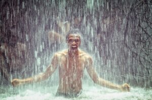 A delighted man enjoys the invigorating flow of water under a waterfall, exuding joy and freedom.